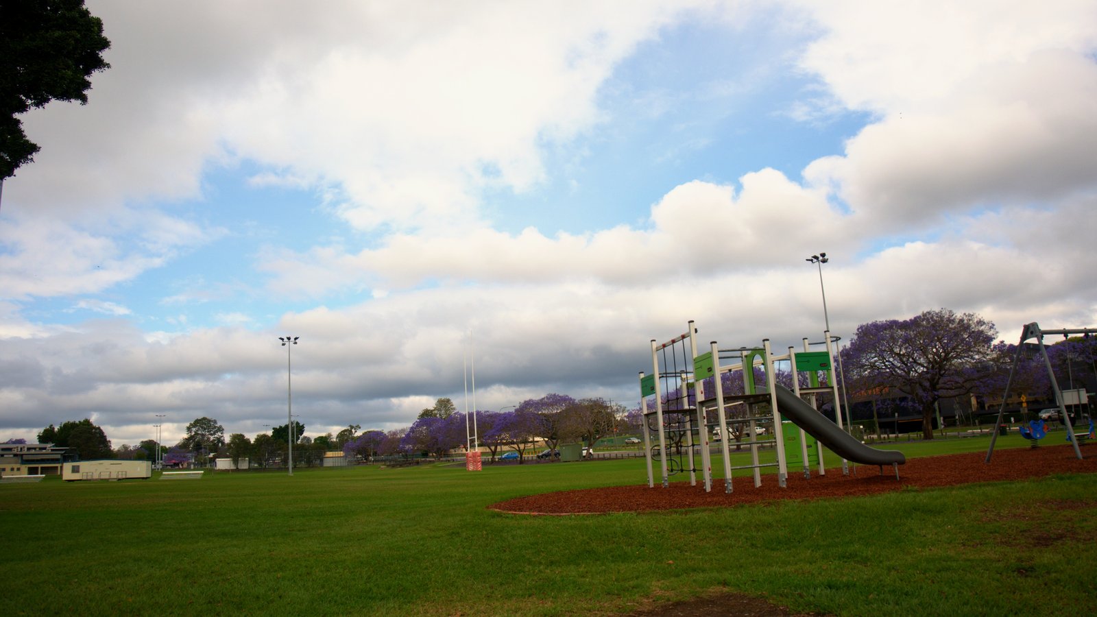 A small playground with slides on a wide grassy park in Goodna under a sky of white clouds