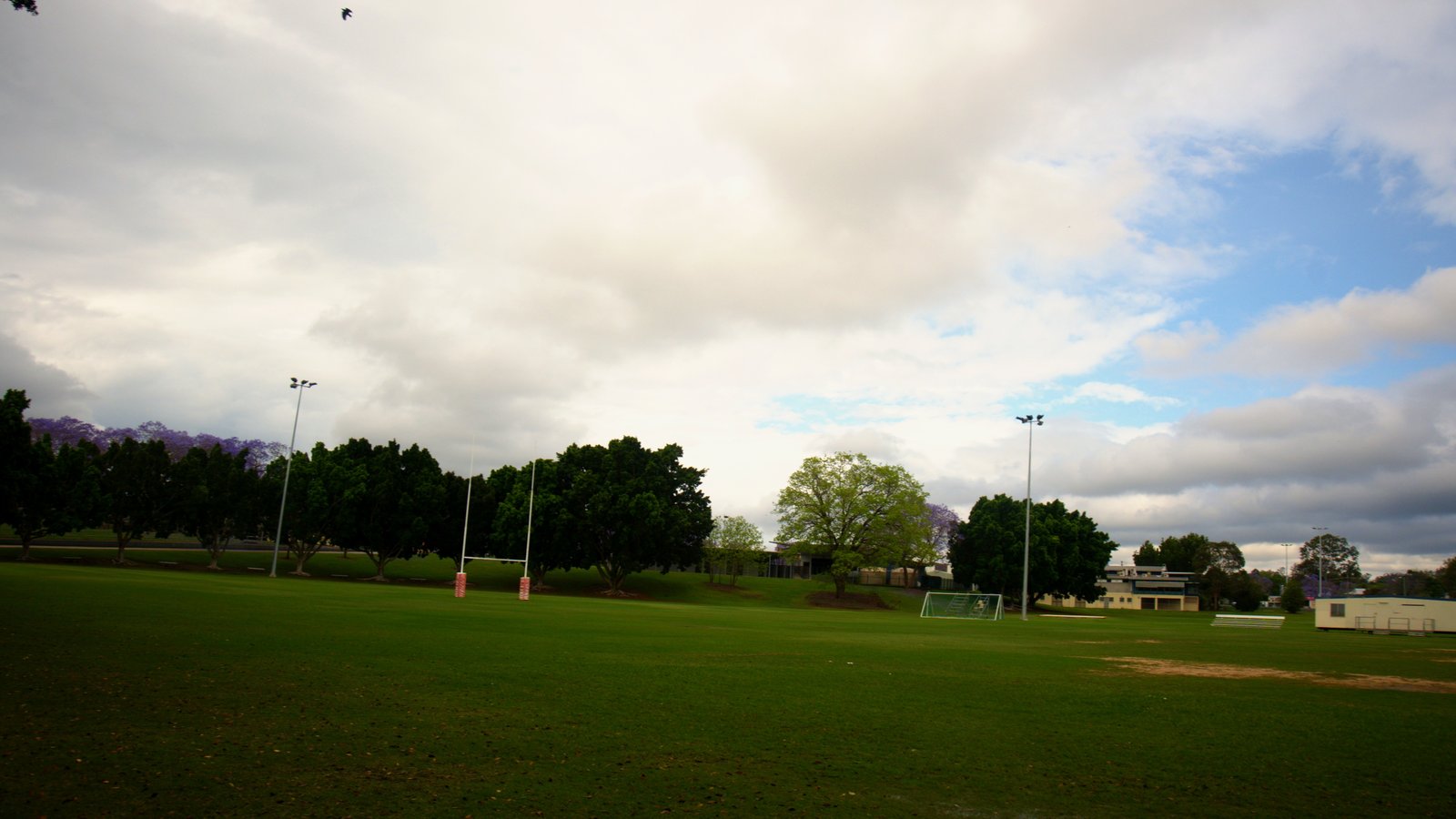 Heavy grey and white clouds over an empty sports field in Goodna with a line of trees on the far side