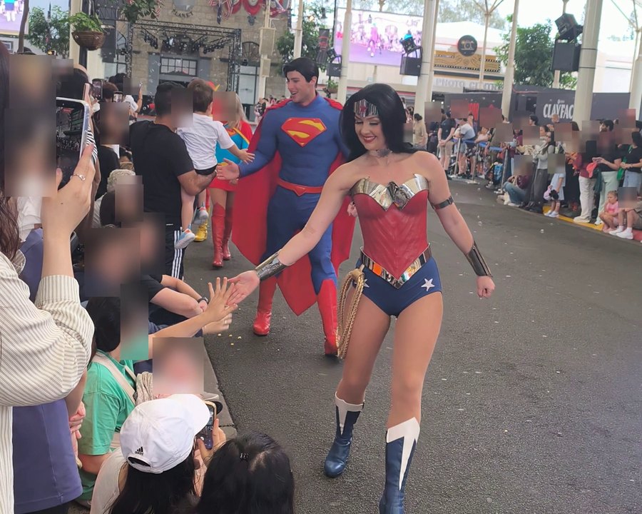 Superman and Wonder Woman high-fiving children in the Movie World Hero Parade under the covered street